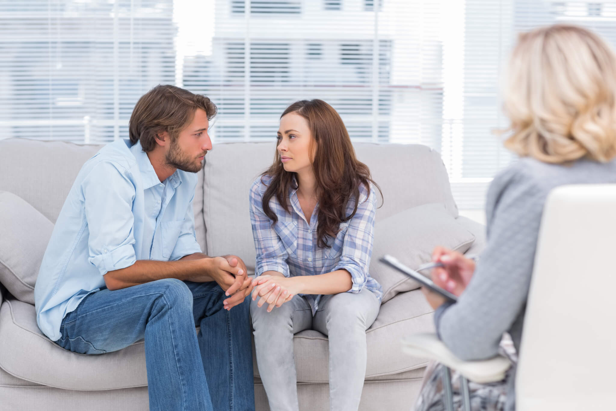 Couple looking to each other during therapy session while therapist watches infidelity recovery